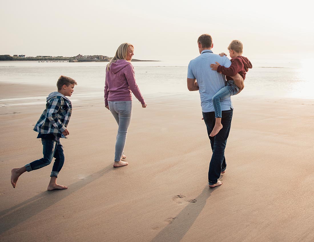 Rear View of family with two children walking down to the waters edge while on holiday.