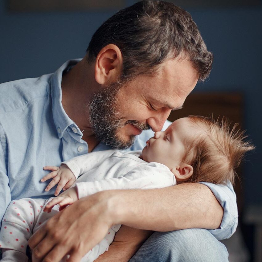 Middle age Caucasian father kissing sleeping newborn baby girl. Parent holding rocking child daughter son in hands. Authentic lifestyle parenting fatherhood moment. Single dad family home life.